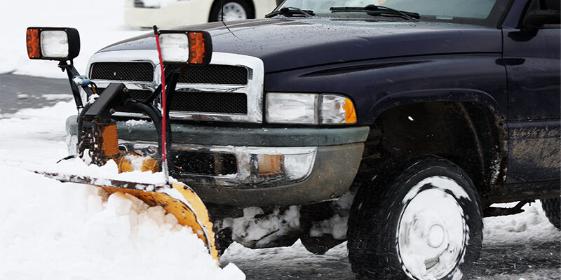 Black truck with plow attached to the front pushing snow